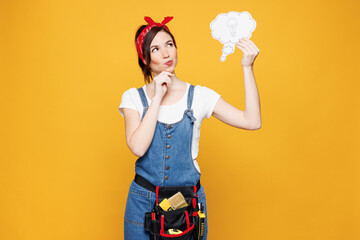 Young employee laborer handyman woman wear overalls belt hold say cloud with lightbulb isolated on plain yellow background. Instruments accessories for renovation apartment room. Repair home concept.