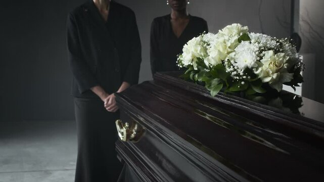 Pallbearers in black carrying dark wooden coffin, decorated with white flowers, at solemn funeral service