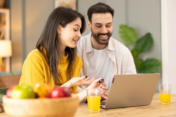 A vibrant young couple engages joyfully over breakfast while working on a laptop, symbolizing...