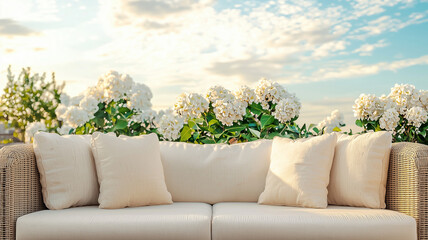 Beige rattan outdoor sofa with white cushions and blooming hydrangeas, elegant patio lounge decor, summer garden furniture inspiration, daylight scenic relaxation concept