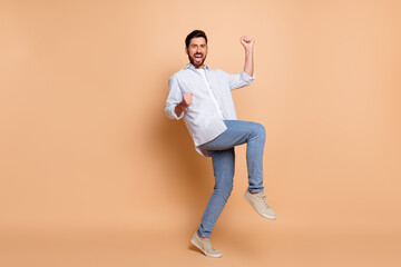 Young man excitedly celebrates while posing against a beige background wearing a casual blue...