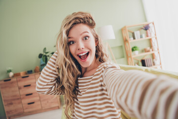 Joyful young blonde woman takes a selfie at home in casual stripes