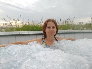 Woman Enjoying Therapeutic Spa Treatment in Outdoor Jacuzzi Surrounded by Natural Landscape