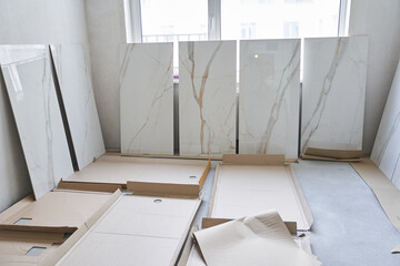 A large marble tile for walls measuring 120 by 60 is displayed in a row, the selection of a pattern on the tile for laying on the walls. On the background of a window under daylight.High quality photo