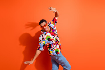 Young male in vibrant print shirt dances energetically against an orange background, showcasing...