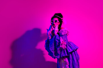 Elegant woman in royal costume posing in vibrant neon lighting with a pink backdrop