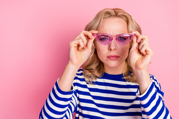 Charming blonde woman wearing striped pullover and pink sunglass posing stylishly against a vibrant pastel pink background