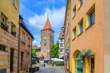 Narrow pedestrian street with old colorful buildings medieval houses and Tiergartnertor Tiergarten Zoo gate tower of city wall in old town Nuremberg city center, Middle Franconia region, Germany