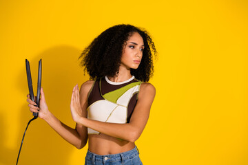 Stylish young woman with curly hair posing against yellow background expressing individuality and...