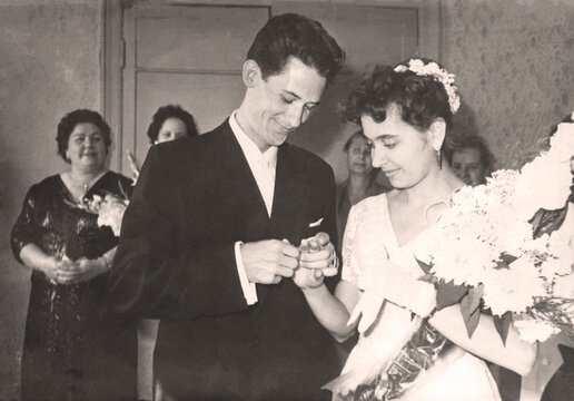 Chasov Yar, USSR - circa 1960: Vintage portrait of the bride and groom. The groom puts a ring on the bride at the registry office. Retro photo.