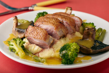 Seared duck breast on a bed of creamy potatoes with vegetables and an orange sauce.