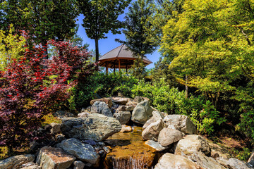 Landscape of a city public free park with a gazebo for relaxation and a flowing stream.