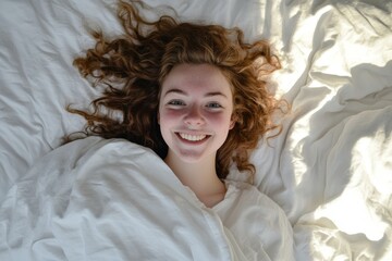 Young woman smiling in bed under a white duvet