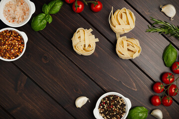 Uncooked pasta and vegetables cooking background, top view, copy space. Italian pasta, tomatoes, basil herbs and spices, italian cuisine concept.