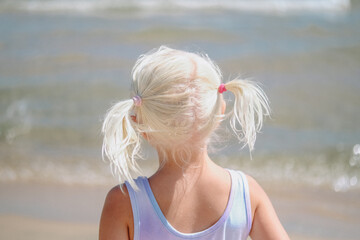Back of a little with blond pig tails on a beach