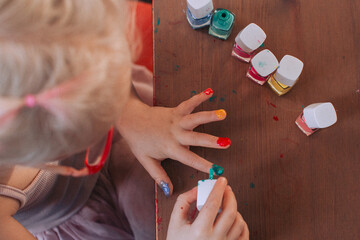 little girl paints her nails with different colors