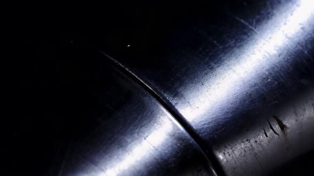 A close up of a silver pipe with a dark background. The pipe is shiny and has a metallic texture