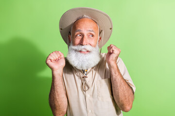 Photo of positive senior traveler man wish raise fists up on summer time voyage isolated green...