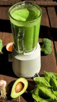 vertical screen: using blender to mix vegan smoothie of broccoli and spinach with addition of avocado and garlic with spicy parika. Diet nutritious green smoothie. Vegetarian drink