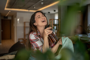 Happy housewife singing and holding cleaning products while tidying up her modern apartment