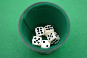 Various white dice with black dots resting inside a green cup se