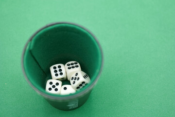 Various dice resting inside a cup on a green felt surface during