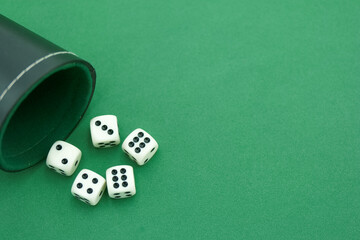 Classic dice rolled out of a leather cup onto a green felt surfa