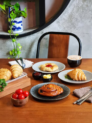 Several freshly baked croissants on a ceramic plate, next to a cup of coffee, a small jar of cream and jam. This image is suitable for cafe menus, food blogs, lifestyle magazines and culinary sites.