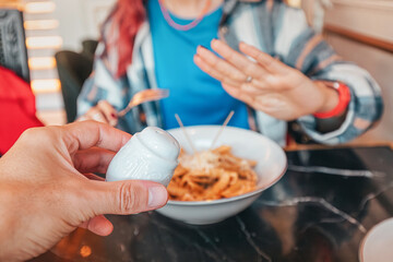 Hand holding salt shaker near plate of pasta and woman making refuse no gesture with hand in...