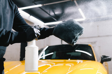 Man sprays wax product on microfiber cloth for car ceramic polishing during detailing procedure. Car cleaning with wax spray on microfiber at the auto service.