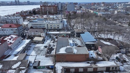 Fototapeta premium Winter aerial view of a city with a mix of old and modern buildings, snowy streets, and parked cars. Some buildings appear under renovation. Bare trees and snow-covered rooftops highlight the cold.