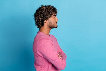 Confident young male with curly hair and stylish pink pullover against a vibrant blue background