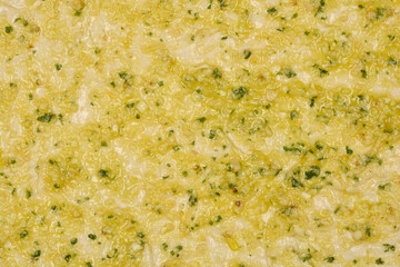 Raw pizza dough topped with pestoClose-up shot of raw pizza dough topped with olive oil, garlic,...
