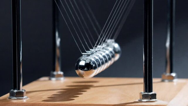 Zeitlupen-Nahaufnahme eines Kugelsto&szlig;-Pendels in Aktion &ndash; sieben Chromkugeln schwingen im perfekten Rhythmus und veranschaulichen die Impuls&uuml;bertragung in der Physik.