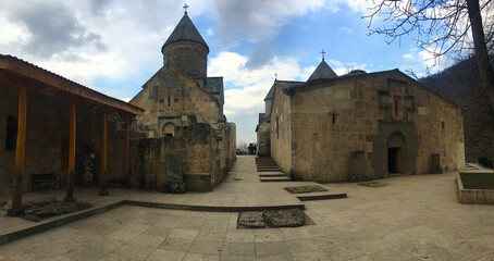 Dome-capped stone buildings clustered around open courtyard beneath cloudy light Architectural ensemble includes bell tower and rounded roofs framed by sparse trees