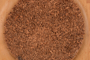 Grated cooking chocolate in a glass bowl, partially visible on a wooden surface, shot close-up