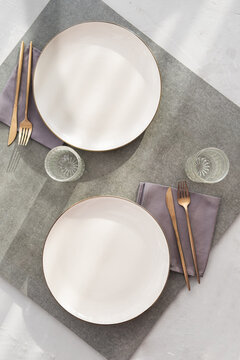 Flat lay of two elegant white porcelain plates with golden forks on table.