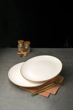 Two white porcelain plates with golden forks on table on black background