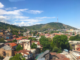 Expansive city view from hilltop with buildings and forest margin beneath clear sky Dense urban...