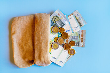 euro money paper bills of 20 euros and 5 euros and many euro coins lie spilled out of a money bag,...