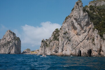 Fototapeta premium Sparkling turquoise waters lap against rugged cliffs and charming Mediterranean architecture in Capri, Italy, as the blue sky and sunlight highlight the island’s romantic coastal allure.