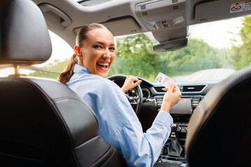 Overjoyed lady sitting in car and showing new driver license, finishing driving school, passed...