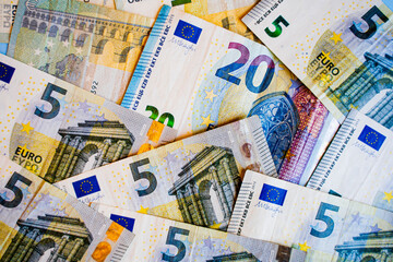euro money paper bills lie all over the frame, occupying the entire frame there are EU money, in denominations of 5 euros and 20 euros, background, in a chaotic order bright bills