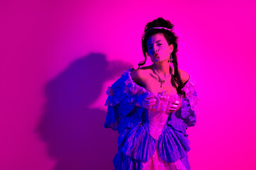 Elegant woman in vintage royal costume posing against vibrant pink neon background