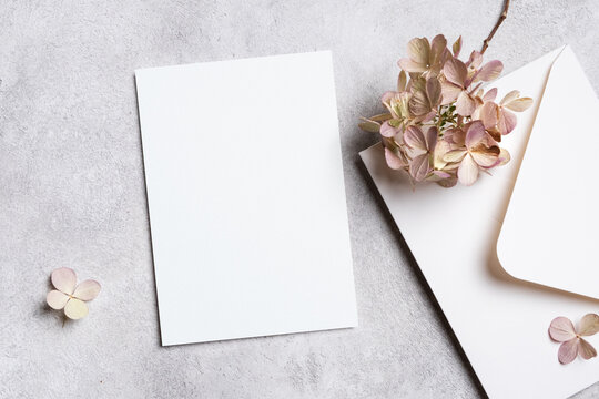 Wedding invitation card mockup with white envelope and dried flowers decor, blank paper card mock up with copy space on grey background