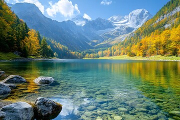 Lake surrounded by mountains and trees with autumn foliage under a blue sky.