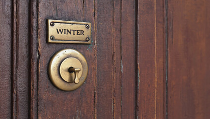 Elegant brass nameplate with 'WINTER' inscription on a weathered wooden door, complemented by a matching brass lock, creating a timeless aesthetic