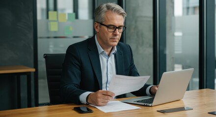 Fototapeta premium Focused Middle-Aged White Man of European Descent in Business Suit Reviewing Documents at Modern Office Desk