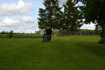 Grandson and grandfather spending time outside together. Toddler boy with balanced bike and grandpa talking to each other. Two generations playing in village