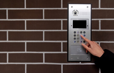 Hand entering code on keypad at building entrance. Space for text.